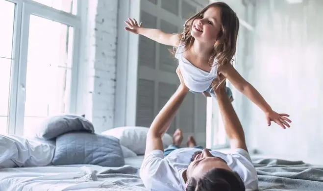 A man and his daughter playing on the bed.