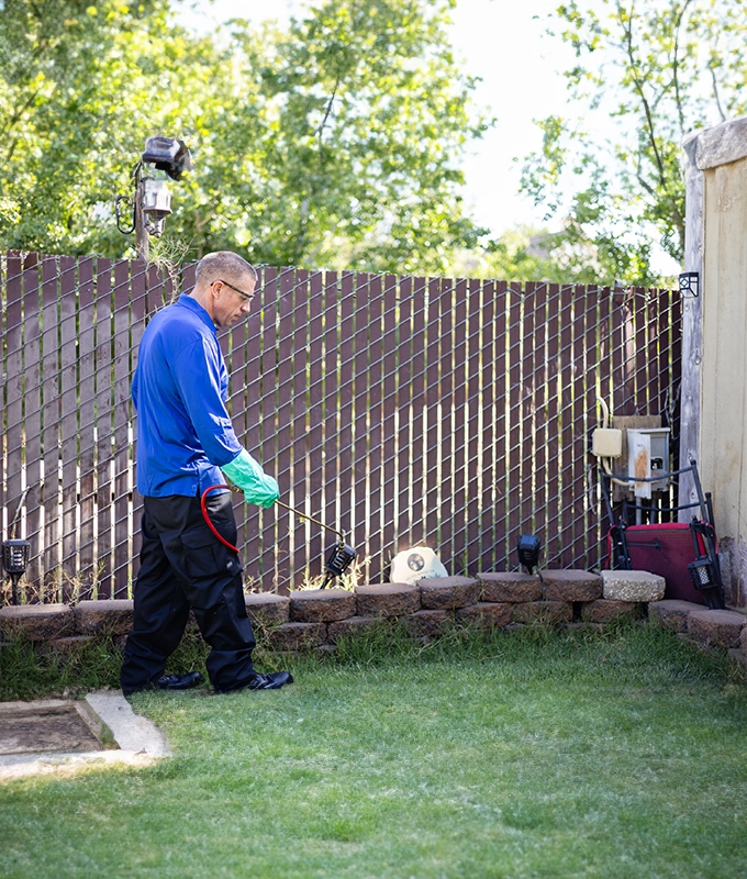 A man in blue shirt and green gloves standing next to a fence.