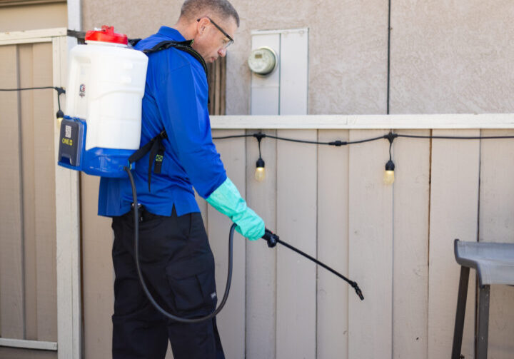 A man in blue jacket spraying water on the ground.